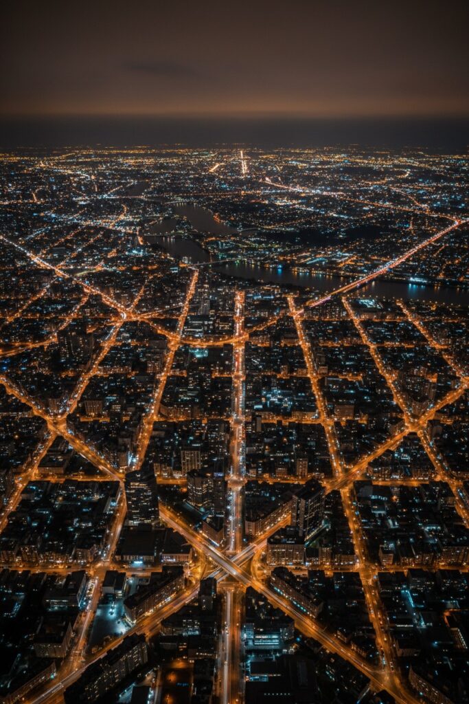 Ein nächtlicher Blick aus der Vogelperspektive auf eine weitläufige Großstadt mit leuchtenden Straßen und Gebäuden, die sich im Raster bis zum Horizont erstrecken.